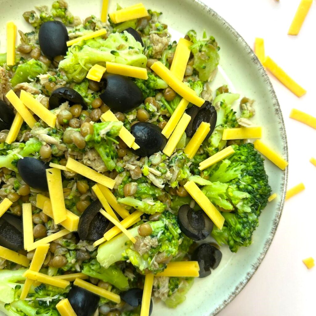 half bord glutenvrije broccolisalade op roze achtergrond met snippers cheddar cheese.