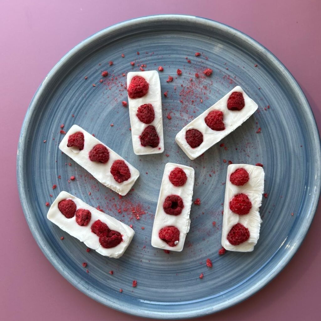 6 glutenvrije yoghurt ice barks op een blauw bord en roze achtergrond.