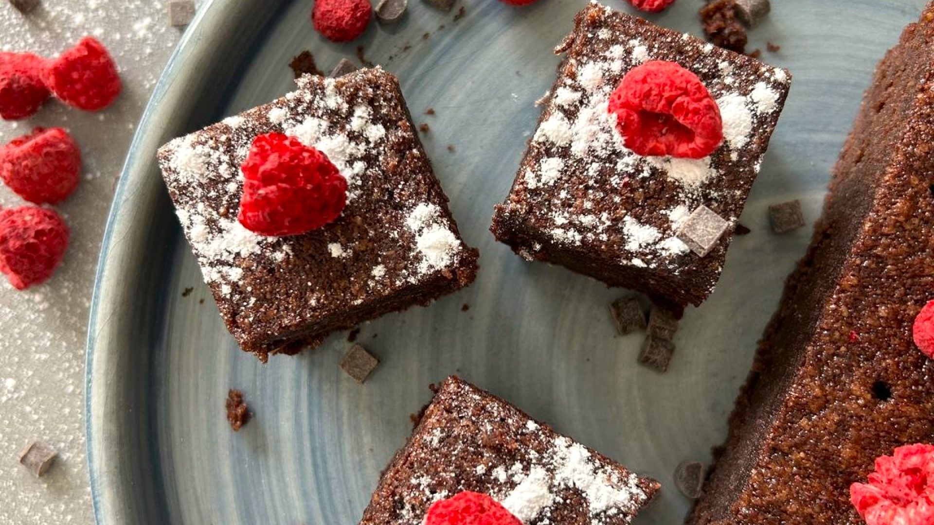 een bord met glutenvrije brownies bedekt met poedersuiker en framboos