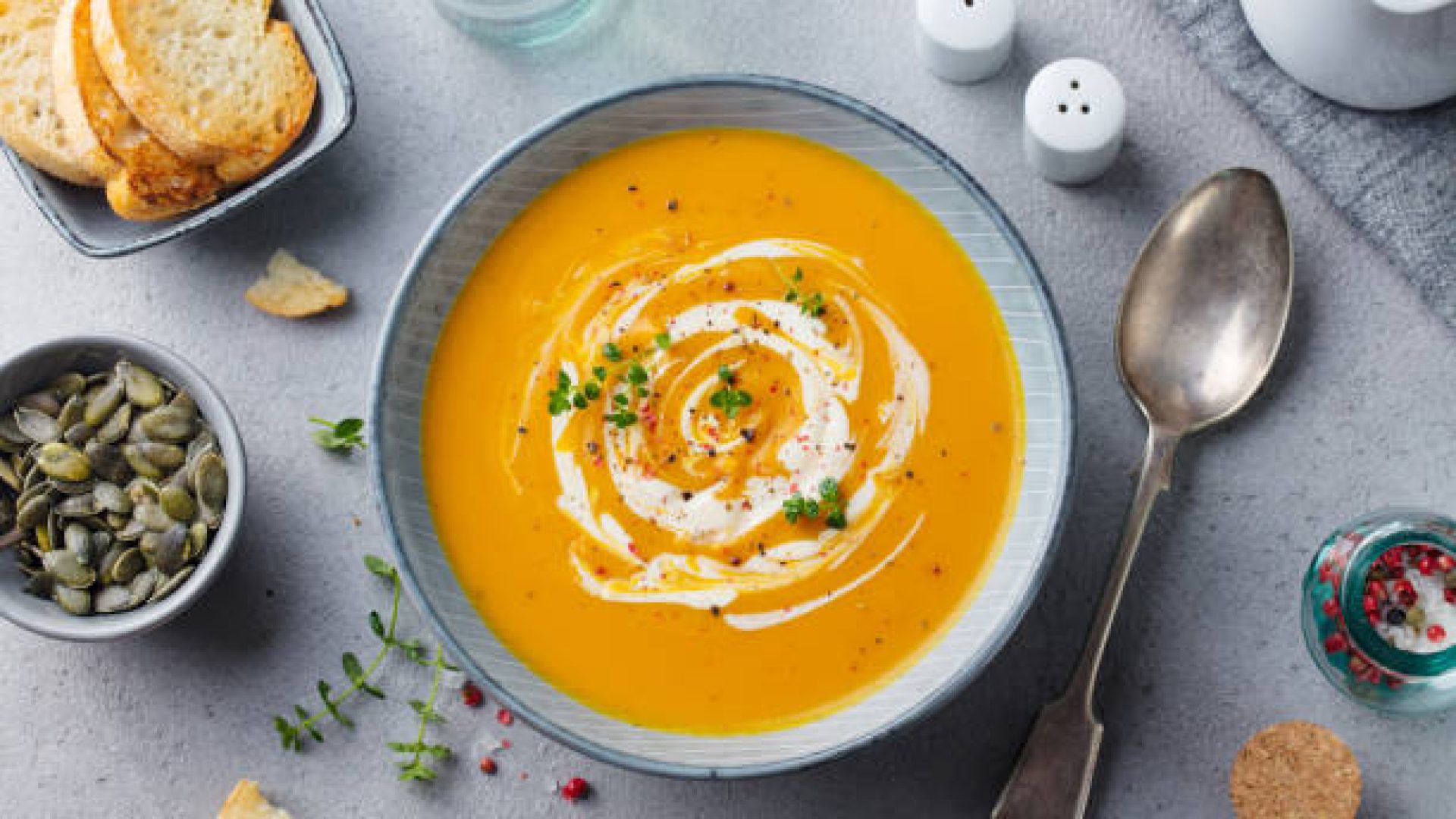 Pumpkin and carrot soup with cream on grey stone background. Top view Pumpkin and carrot soup with cream on grey stone background. Top view